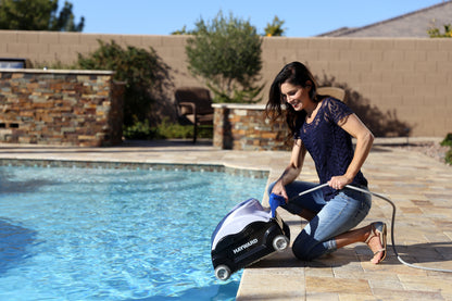 A person placing the Hayward SharkVac XL (W3RC9740WCCUB) robotic cleaner into an in-ground pool for floor and wall cleaning.