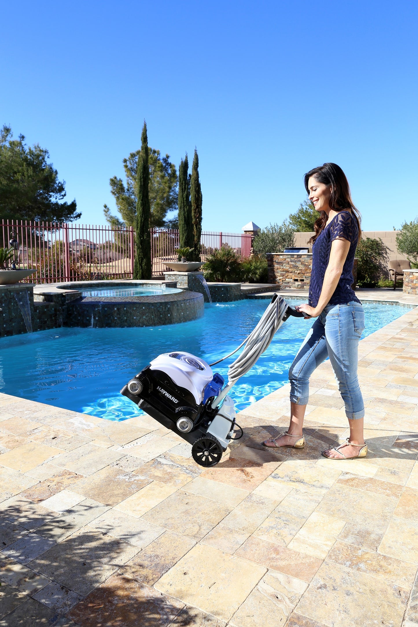 A person easily transporting the Hayward SharkVac XL (W3RC9742WCCUBY) robotic cleaner using the included rolling caddy cart next to an in-ground pool.